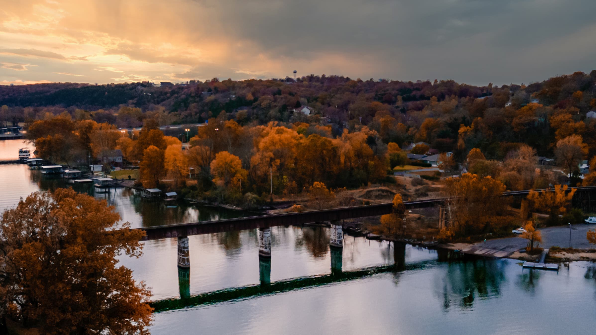 Aerial view of Lake Taneycomo at sunset with reflections of autumn trees and a bridge crossing the water in Branson, Missouri.