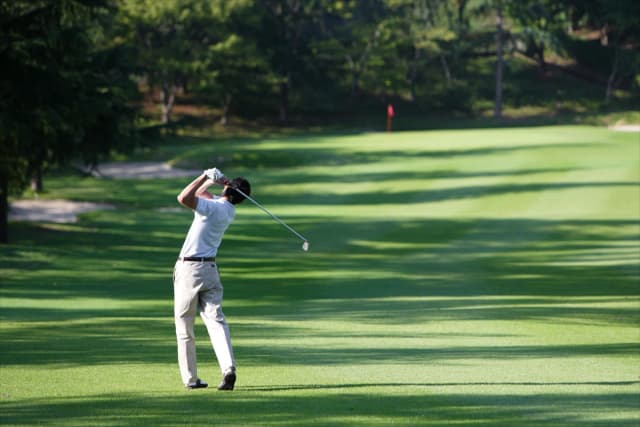 Golfer swinging on a lush green course in Branson, Missouri with trees and sunlight in the background.