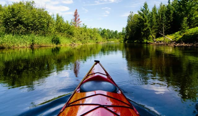 Red kayak gliding across a calm river surrounded by lush green forest near Branson, Missouri.