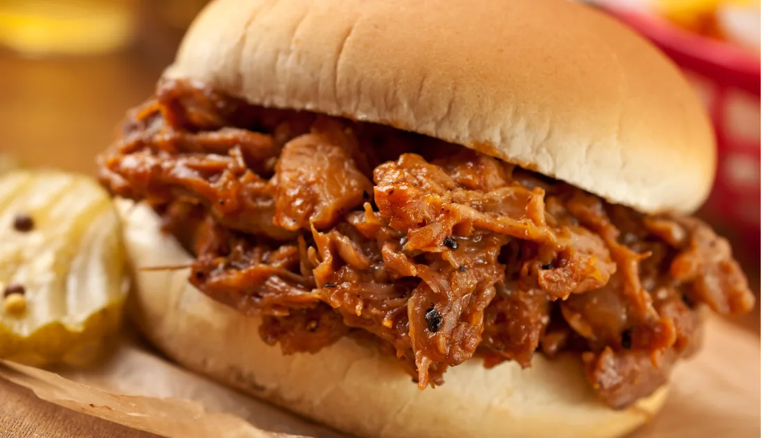 Close-up of a pulled pork sandwich with barbecue sauce served with sliced pickles in Branson, Missouri.