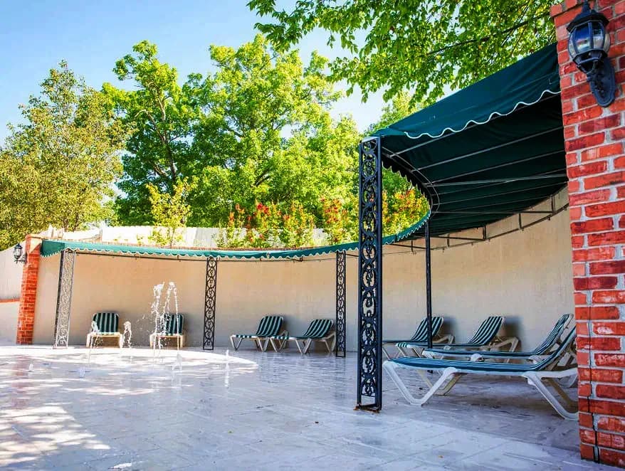 Outdoor shuffleboard courts with green benches beside a clubhouse and landscaped greenery on a bright day.