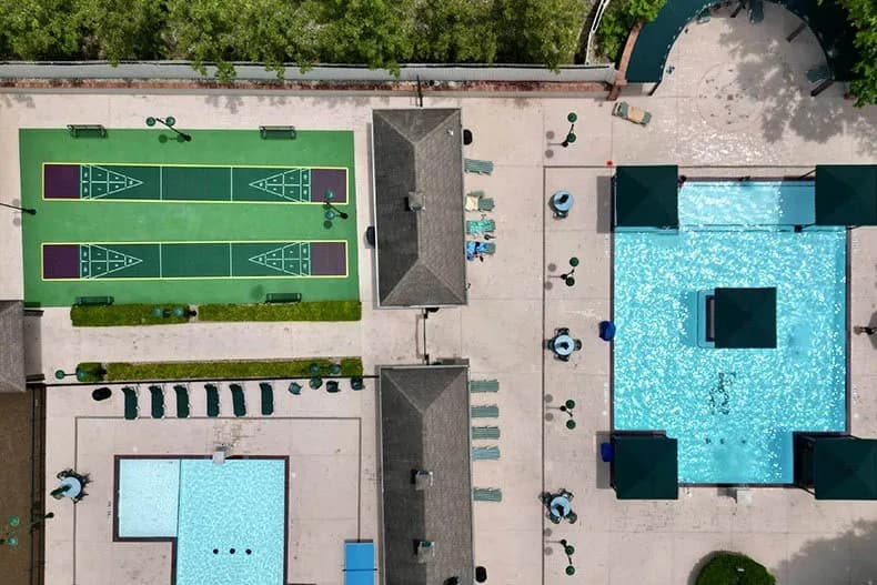 Top-down view of a bright blue swimming pool with green umbrellas, lounge chairs, and people enjoying the water.