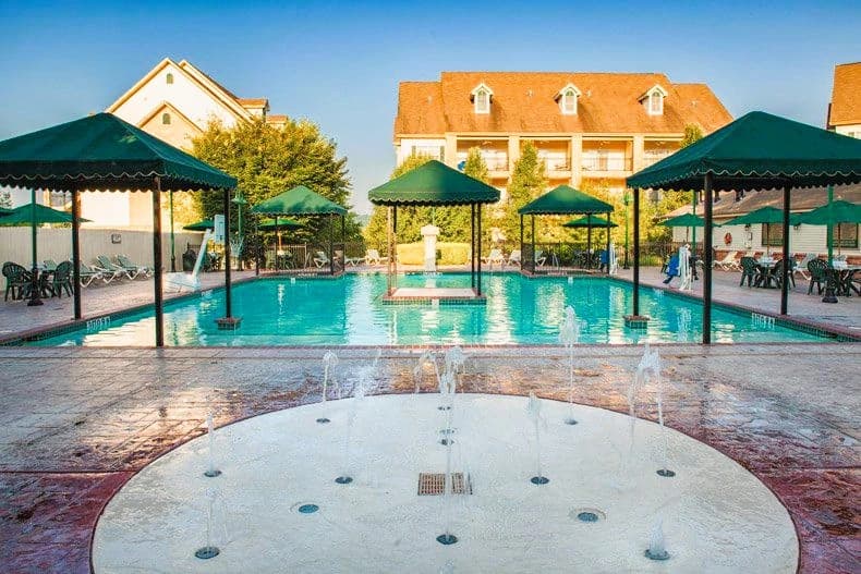 Wide view of resort pool area with water features and shaded seating under green canopies at French Quarter Resort.