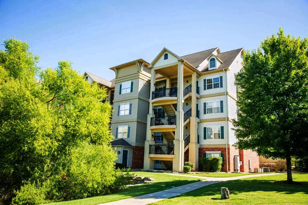 Four-story apartment building with balconies and lush green landscaping.